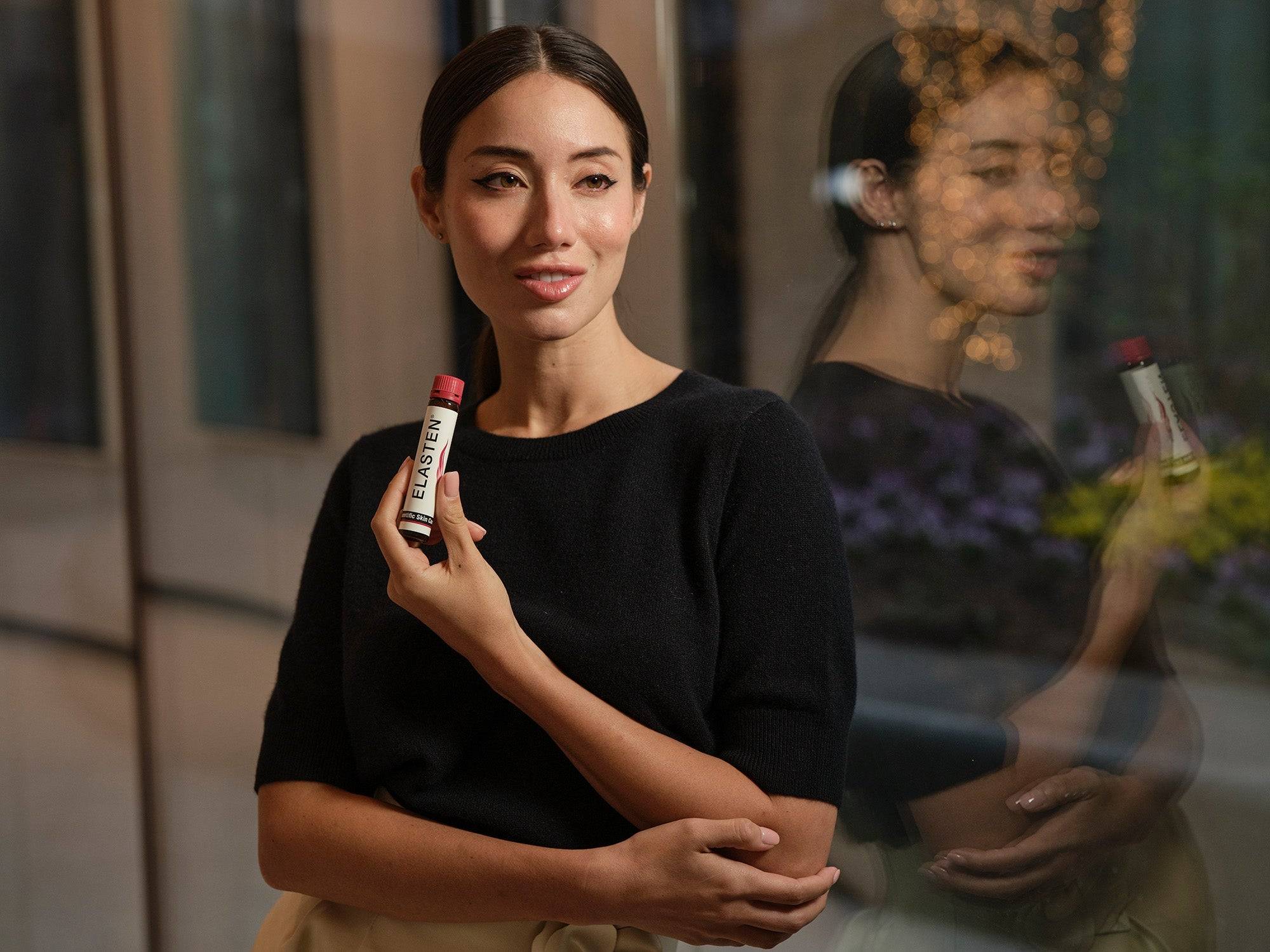 Asiatische Frau hält ELASTEN® Trinkampulle in der Hand und präsentiert sie in die Kamera.