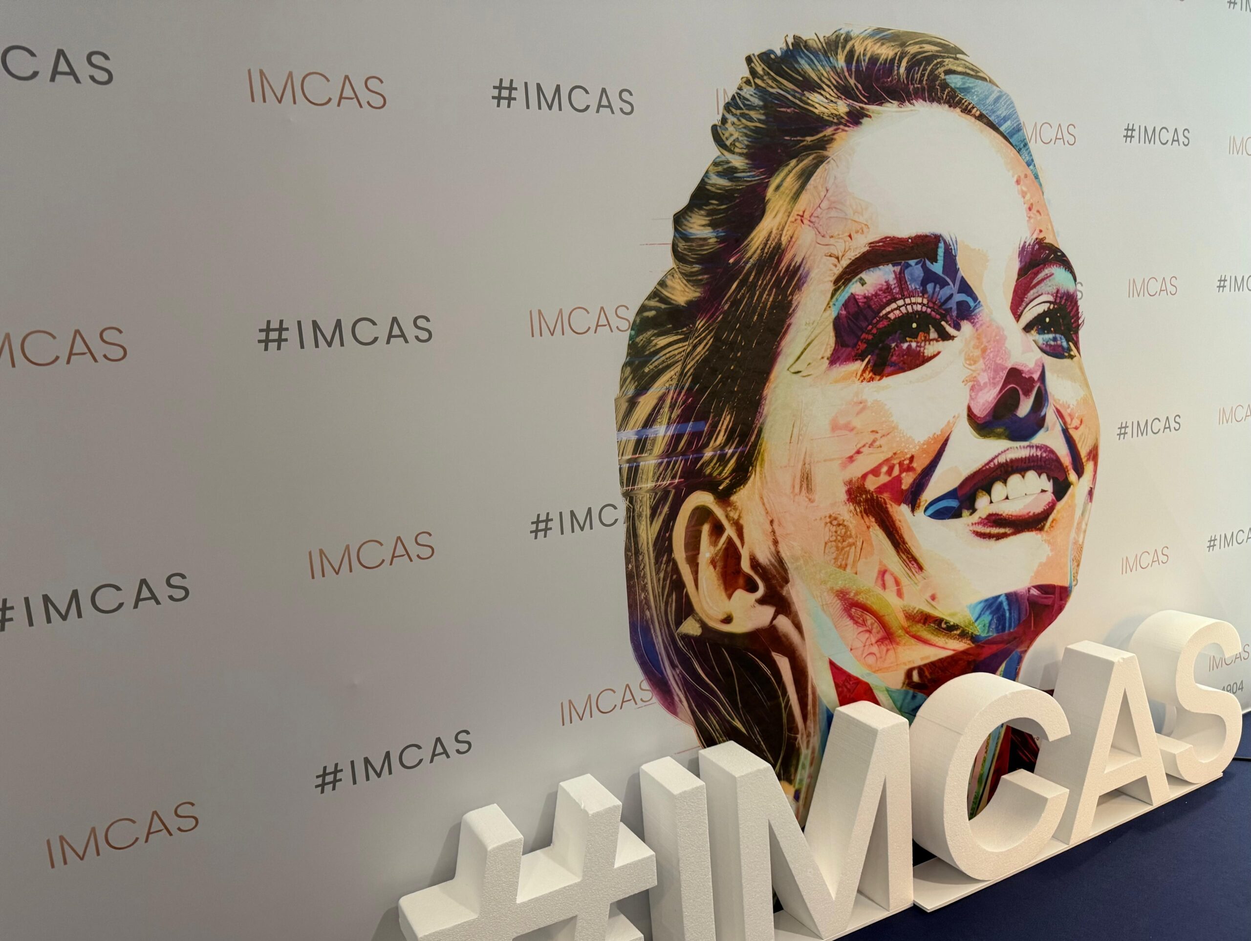 Frauenkopf auf Werbewand abegbildet mit den Schriftzügen #imcas. Vor der Werbewand steht noch ein 3D-Modell des Schriftzugs #imcas.